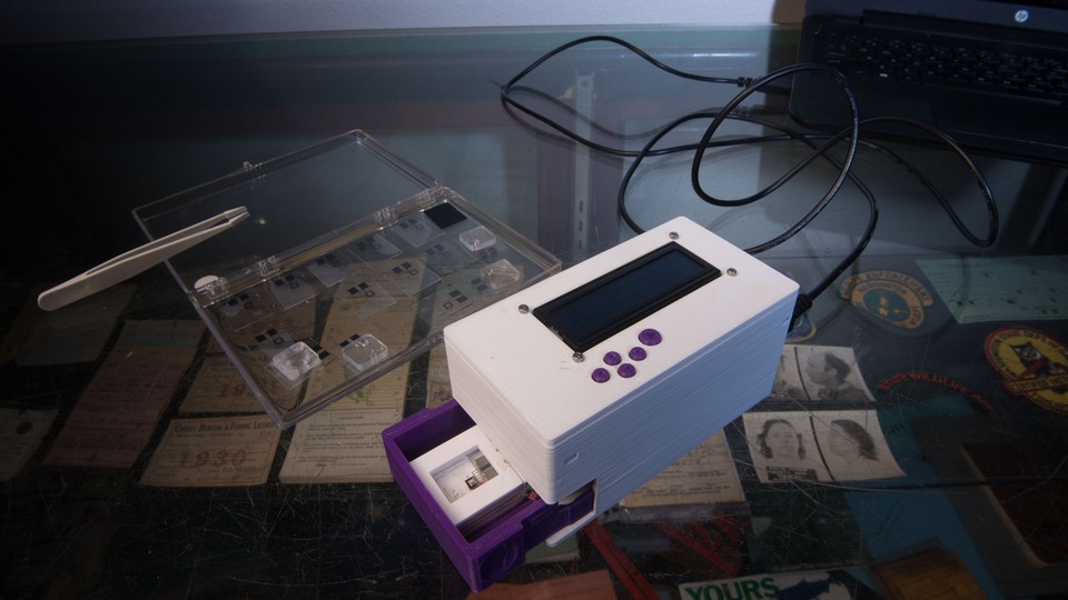 A Nintendo-like box-shaped electronic device next to a plastic tray with tweezers and samples