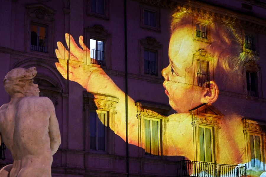 The image of a painting of a child is projected onto the wall of a building.