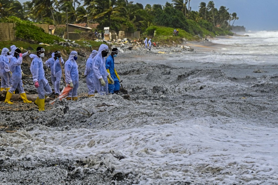 Soldiers wearing protective gear wade through thick piles of plastic debris floating in waves as they crash ashore.
