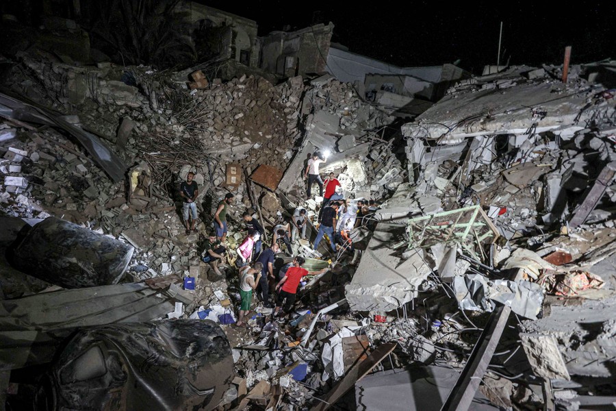 A small group of people stand in a crater among huge piles of rubble from a destroyed building.