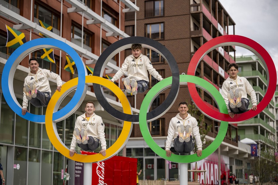 Five gymnasts pose with an Olympic-ring structure.