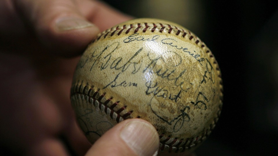 A close-up of a person holding a baseball signed by Babe Ruth and Lou Gehrig.