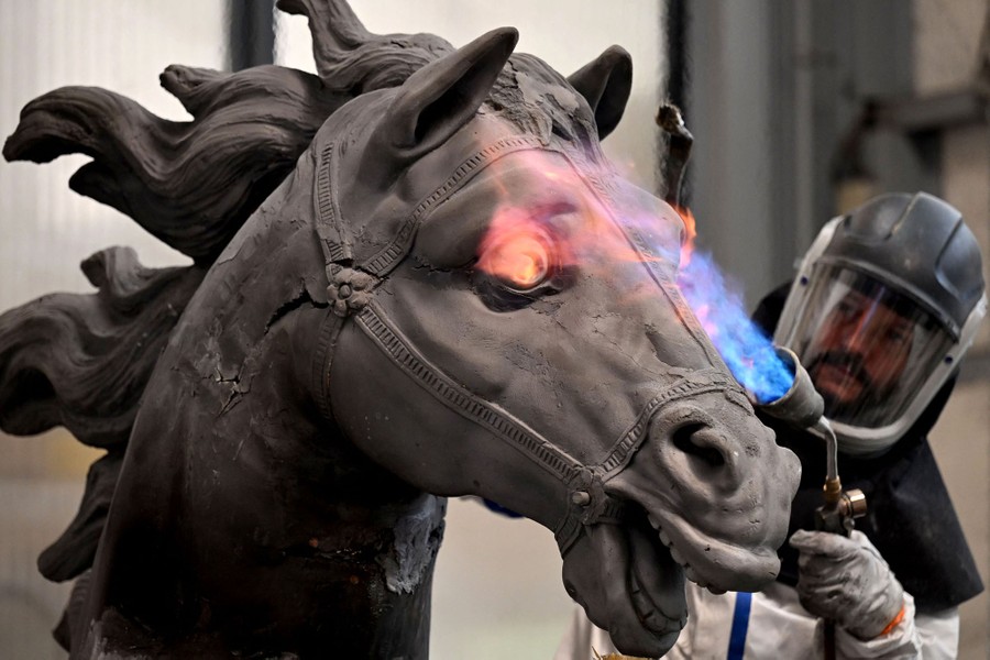 A worker uses a torch to restore part of the head of a large metal sculpture of a horse.