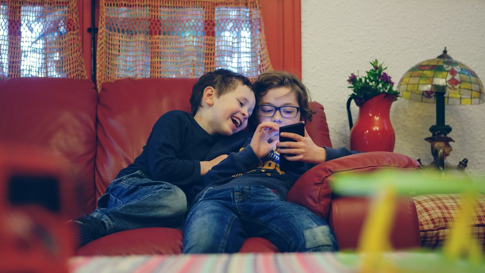 Two kids look at a smartphone at home