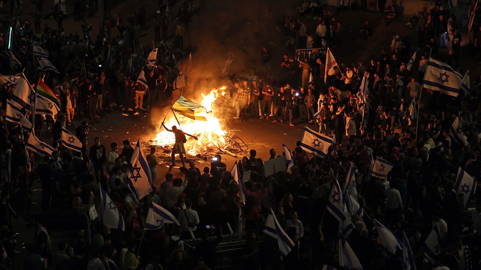 Picture that shows protesters blocking a road and holding national flags as they gather around a bonfire during a rally against the Israeli government's judicial reform in Tel Aviv, Israel, on March 27, 2023