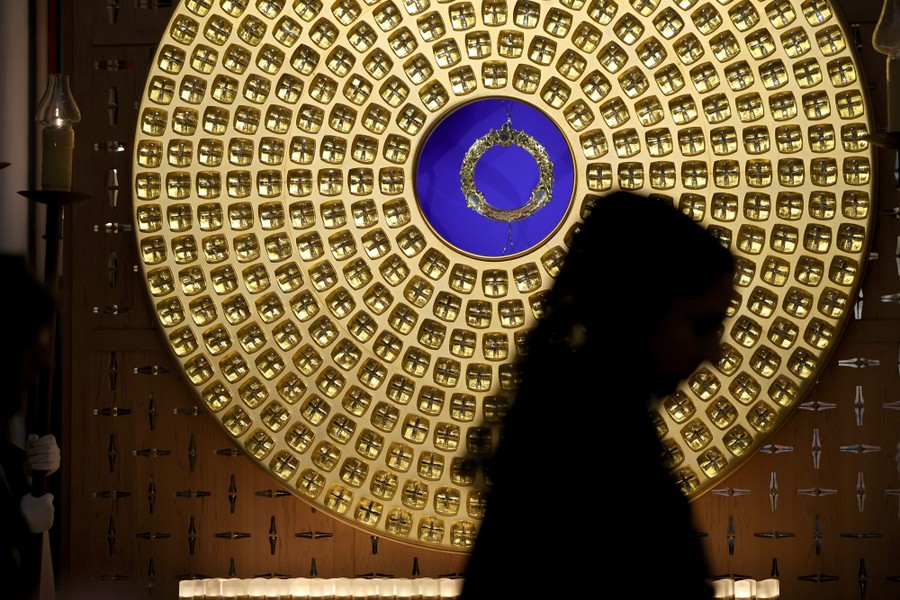A person walks past a large circular golden frame on a wall, surrounding a displayed crown-of-thorns relic.