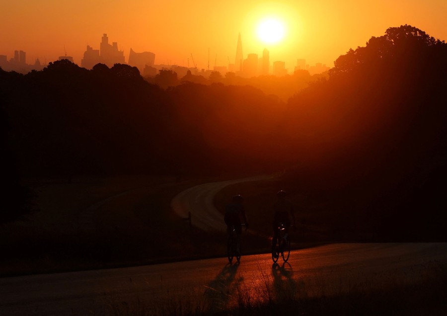 The sun rises above the London skyline as cyclists pass by on a path.