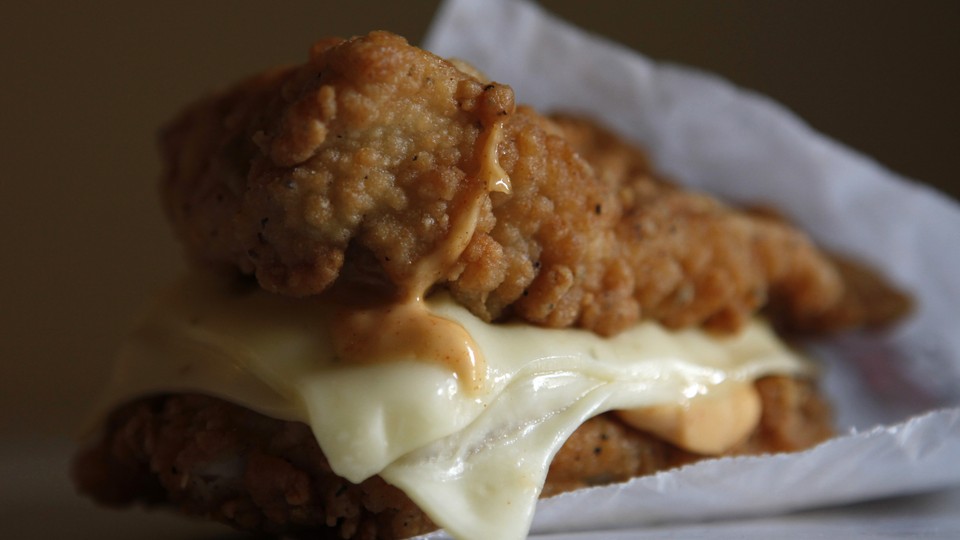 A close-up photograph of a fast-food sandwich made of two chicken tenders with cheese between them.