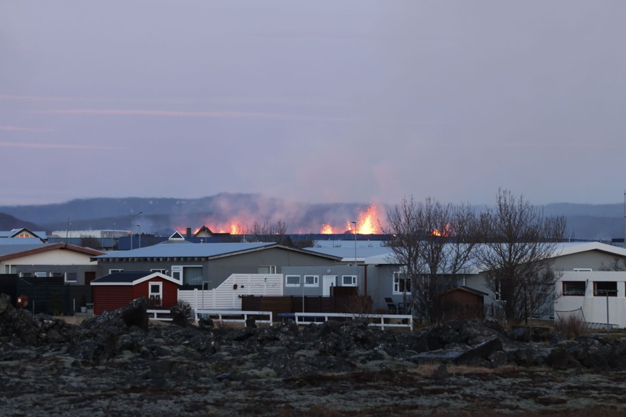 Jets of lava in the near distance, beyond a group of houses