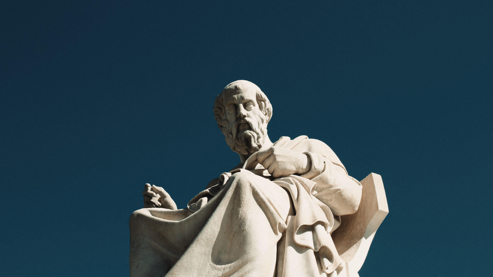 Color photograph of a marble statue of Plato seen in front of a dark-blue background.