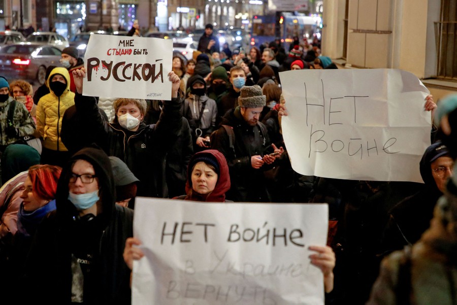 A group of people attend a protest with banners reading (in Russian) "I'm ashamed to be Russian" and "No war"
