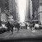 black-and-white photo of NYC street with people running alongside cars