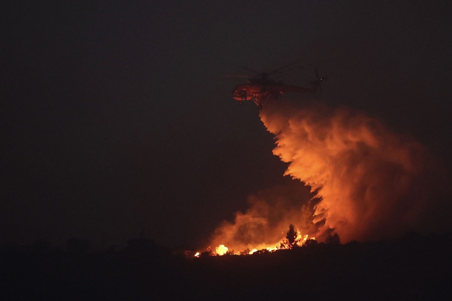 A helicopter drops water onto a wildfire at night.