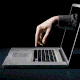 An image of a hand reaching through a laptop screen to type on the keyboard