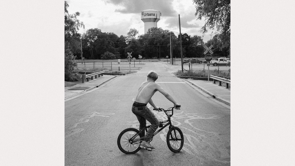 a black and white photograph of a teen boy on a bike near a water tower