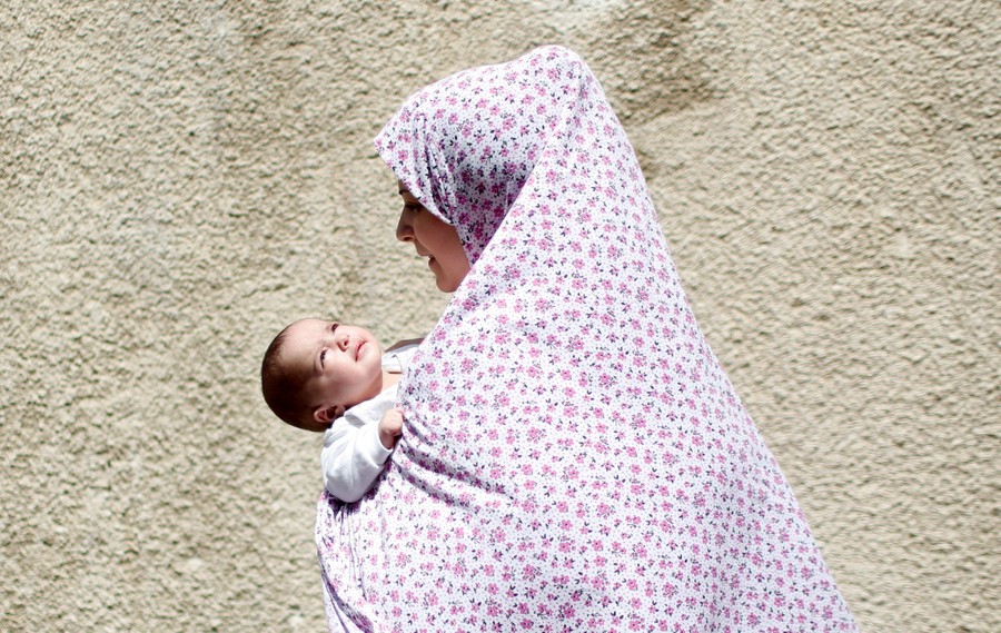 A Palestinian woman carrying a baby evacuates an area after an air strike.