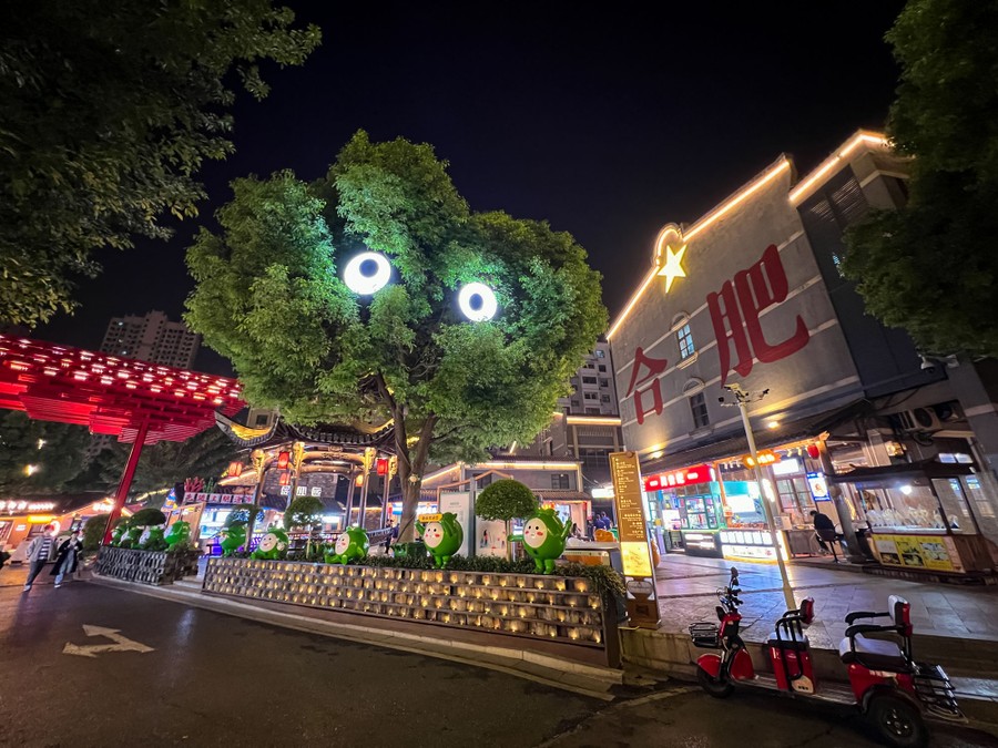 A small tree in a shopping district appears to have two large glowing eyes in it.