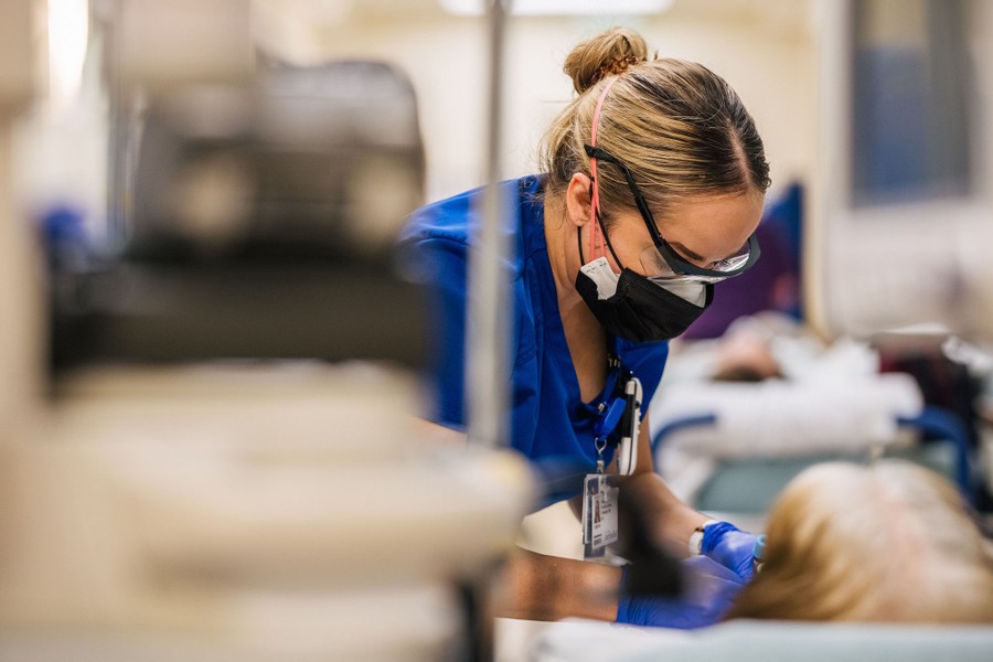 A nurse leans in to treat a COVID-19 patient lying on a gurney in a hallway.