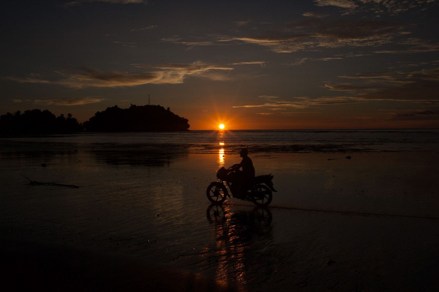 A person rides a motorcycle on a beach at sunset.