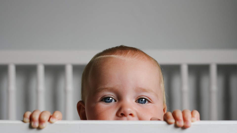 A baby peeks out of a crib.