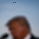 A blurred photograph of Trump speaking into a microphone in the foreground, with an eagle flying above him in the background.