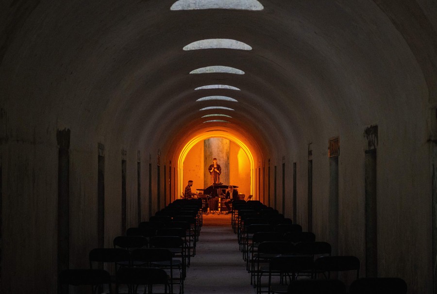 Musicians perform inside a long, arched room.