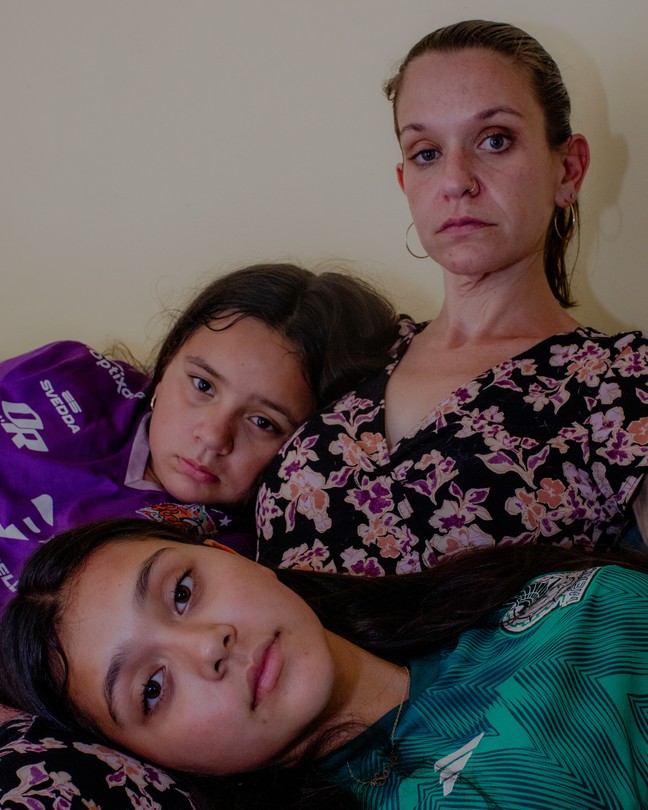 A mom sitting with her two daughters leaning on her