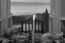 A table set with food and wine and a lit candle, with a door open in the background showing the sky