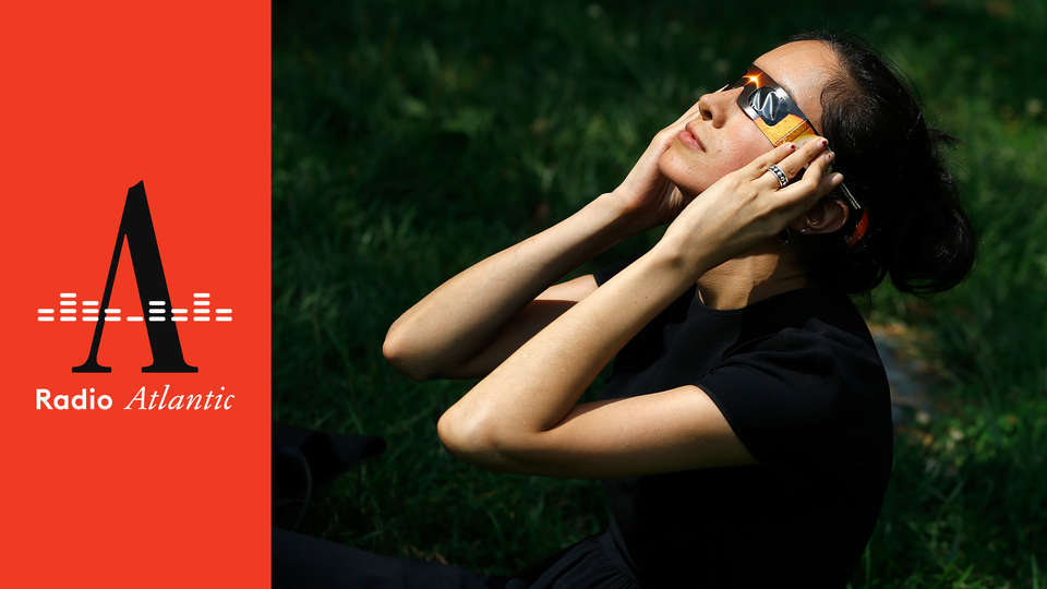 A person wearing eclipse glasses outside looks up toward the sun.
