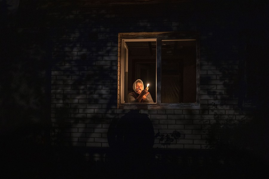 A woman looks out an apartment window while holding a candle at night.