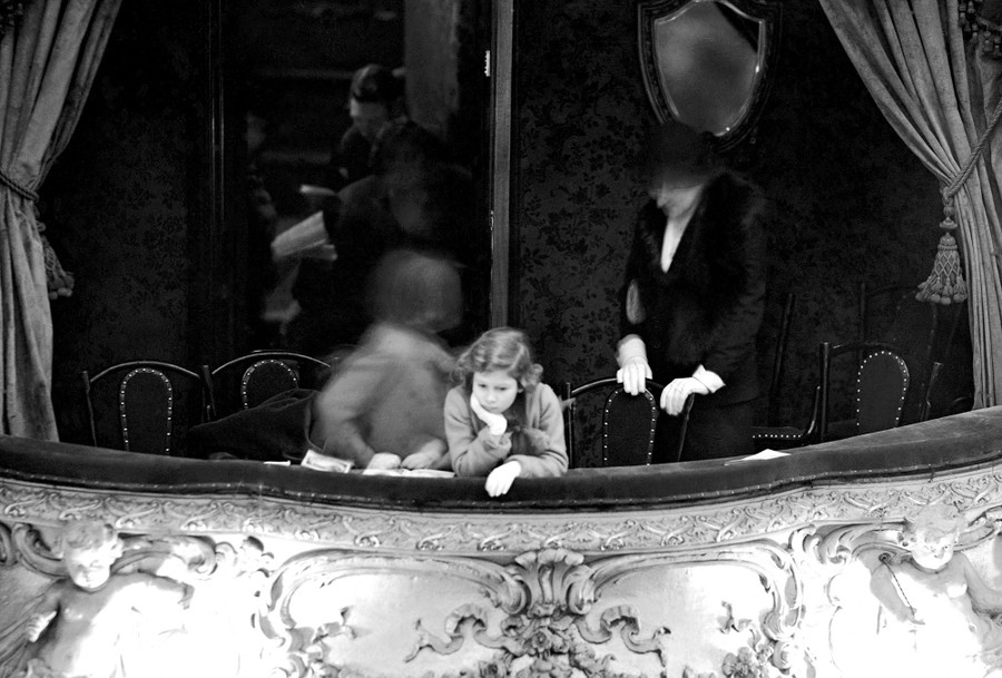 Princess Elizabeth leans over the edge of a balcony seat in a theater.