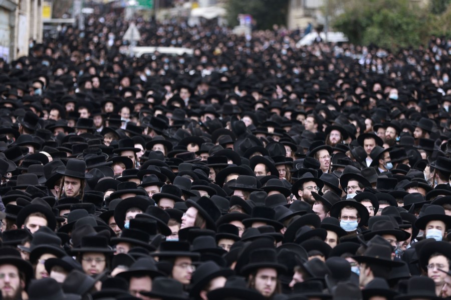 A crowd of men wearing traditional black hats fills a street.