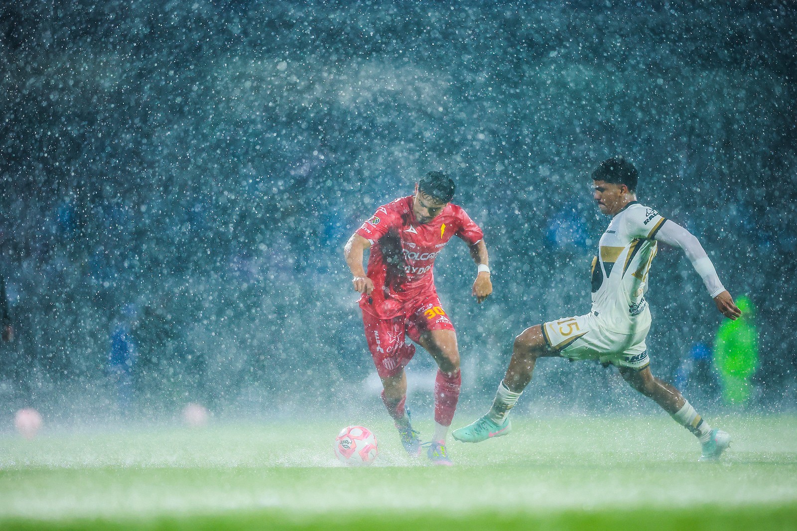 Two soccer players vie for the ball during a match in a rain storm.