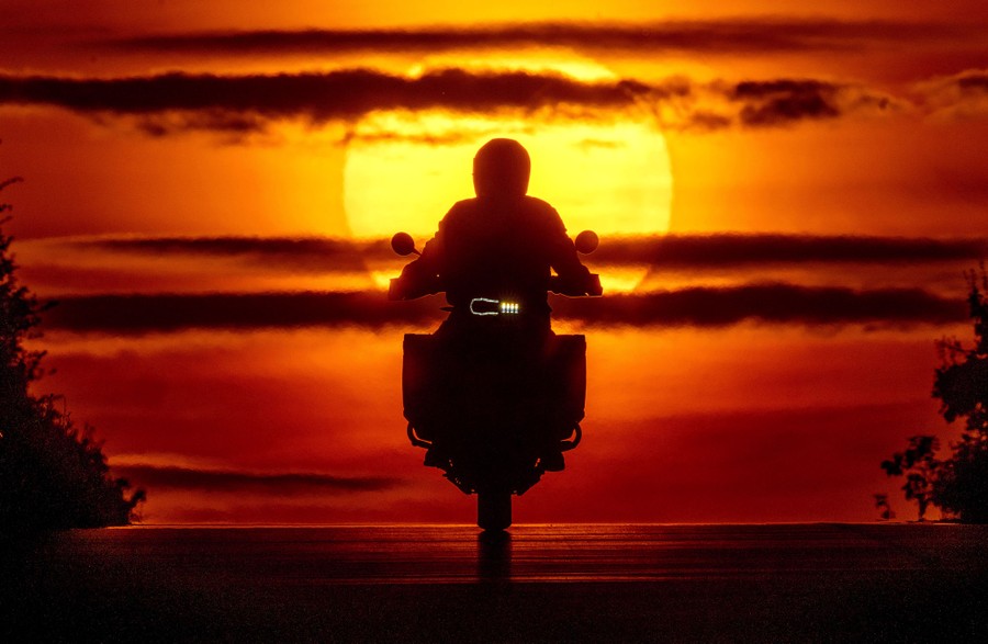 A man on a motorcycle silhouetted by the rising sun