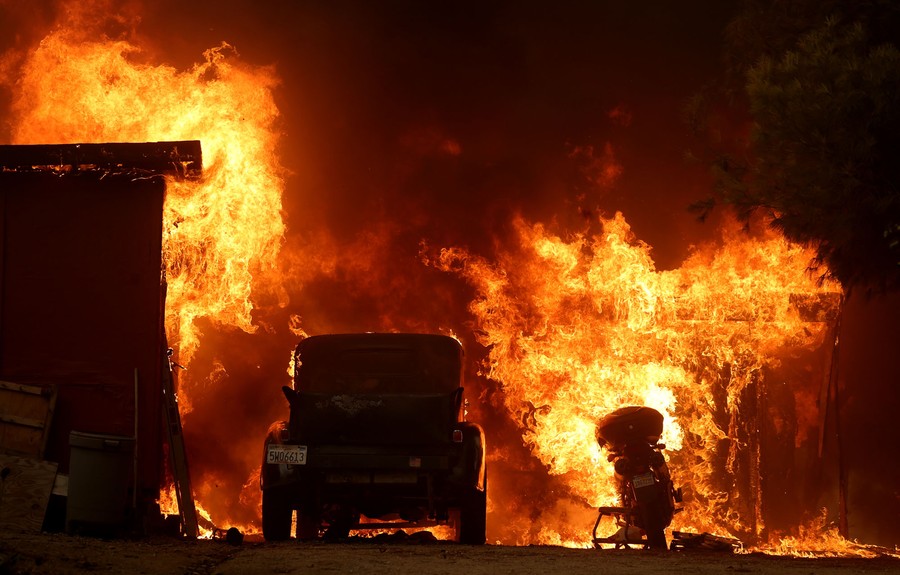 A truck and a scooter go up in flames beside a burning structure.