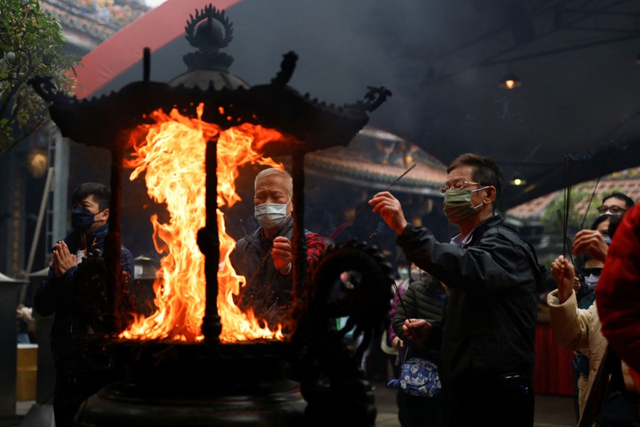 Several people gather at a temple, placing incense into a fire.