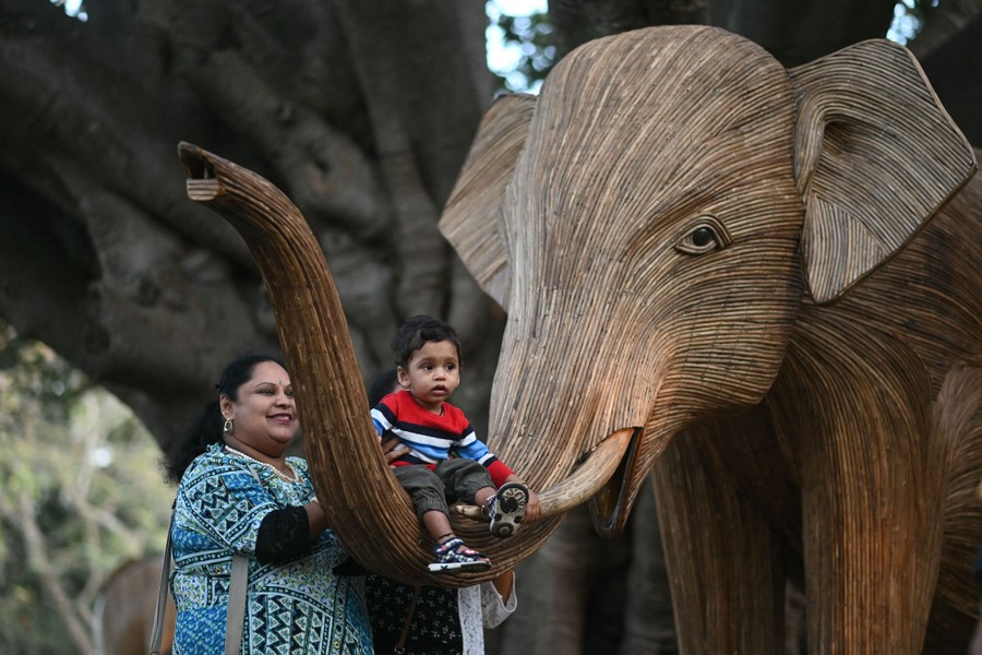 A woman and a child pose in front of a life-size wooden model of an elephant.
