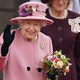 Queen Elizabeth II waving, wearing a pink coat and hat, holding flowers