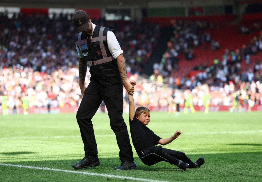 A security officer drags an unhappy boy by the arm, taking him off a soccer field.