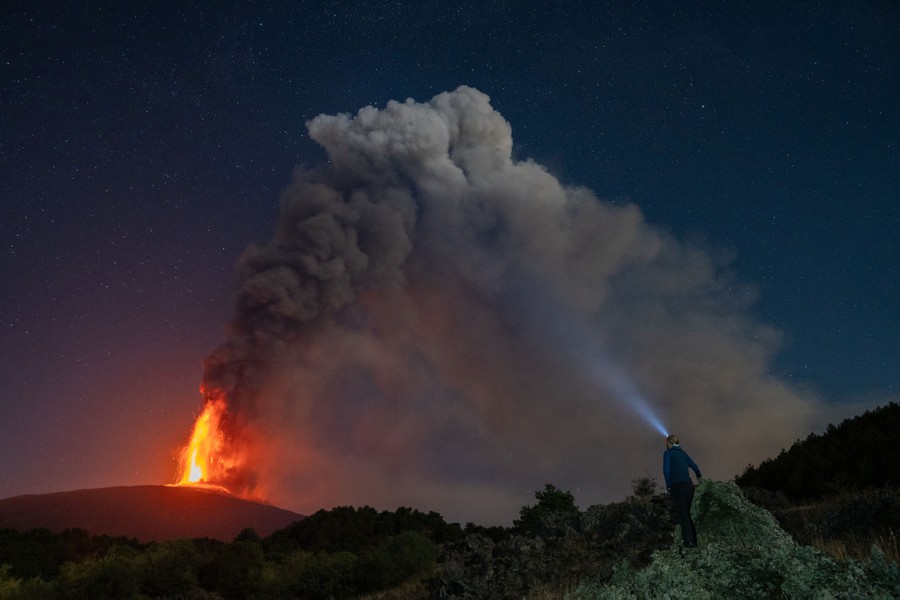 A person watches an eruption from a volcano at night.