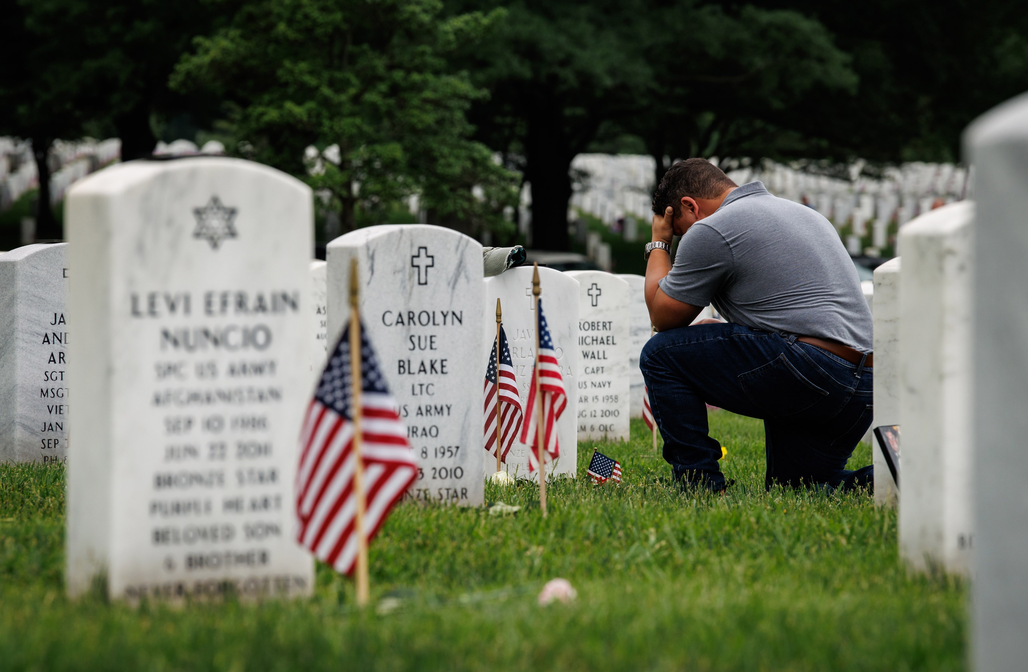 A mourner kneels at the headstone of a fallen loved one in Arlington National Cemetery.