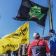 A color photo of a group of protesters carry flags, including an American one and a "Groyper" flag, which shows Pepe the frog on a black background.