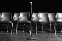 Empty chairs are pictured on a stage behind a standing microphone.