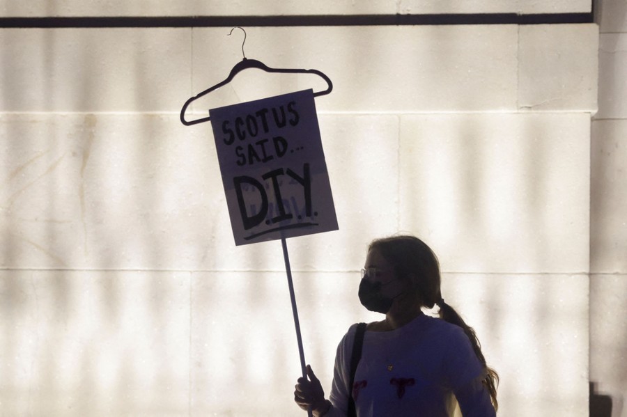 An abortion-rights supporter holds a sign with a clothes hanger attached; the sign reads "SCOTUS said D.I.Y."
