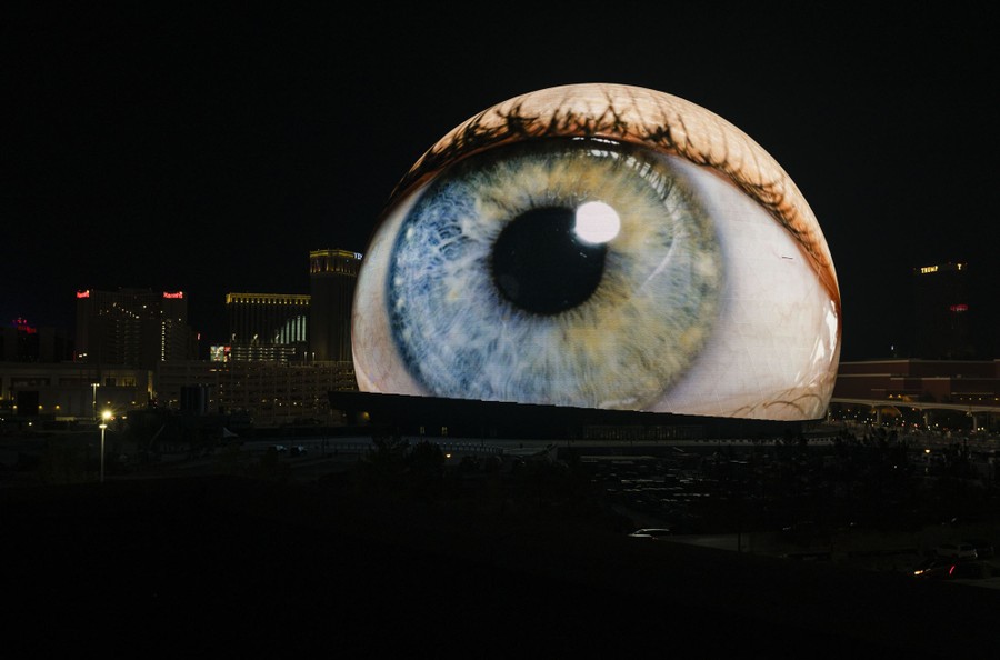 A giant illuminated spherical structure lights up with a video projection of a human eye.