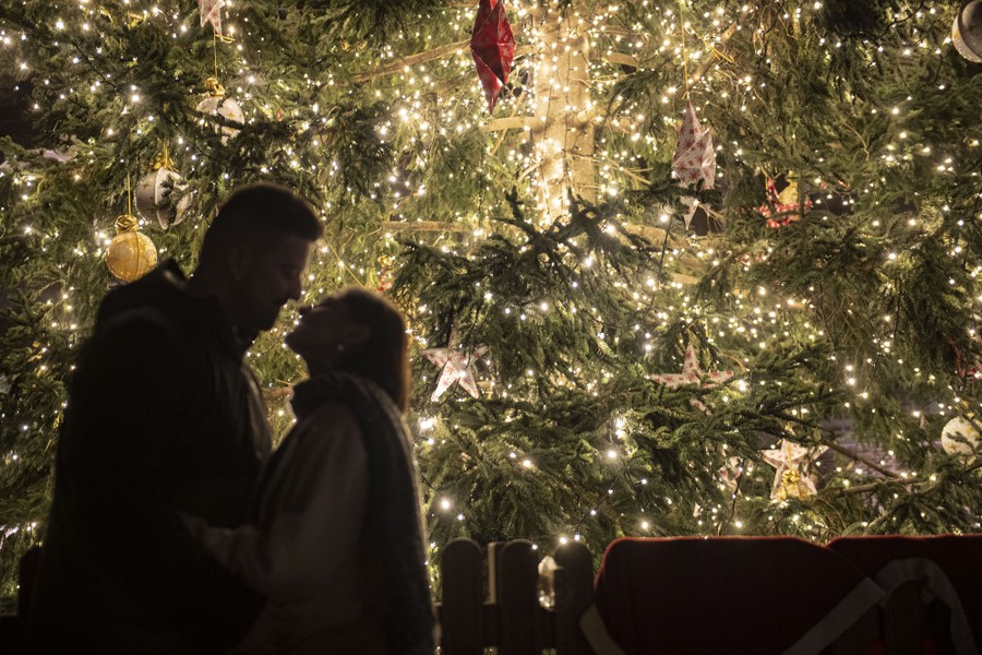 A couple kisses under a Christmas tree.