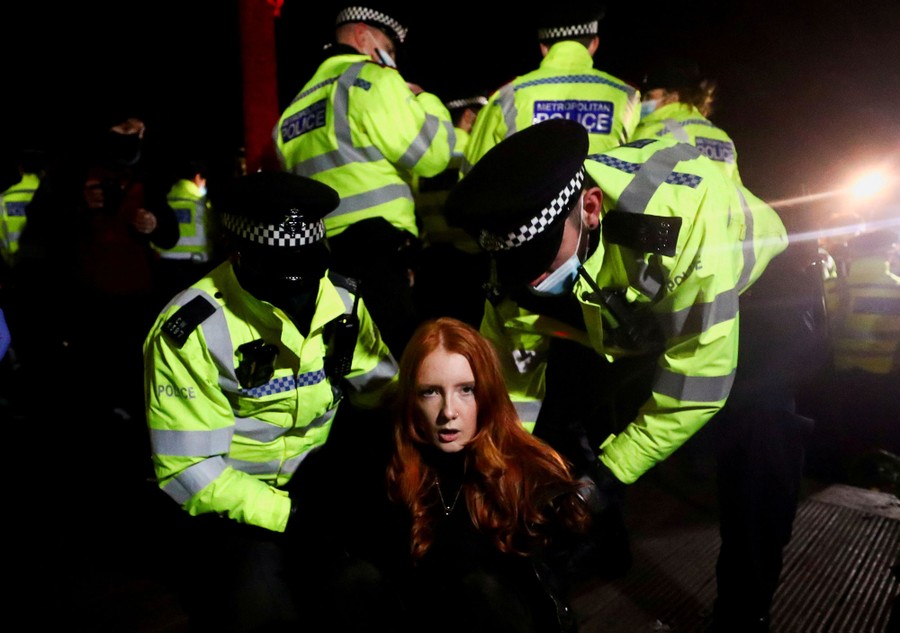 A woman looks toward the camera while she is restrained by police officers.