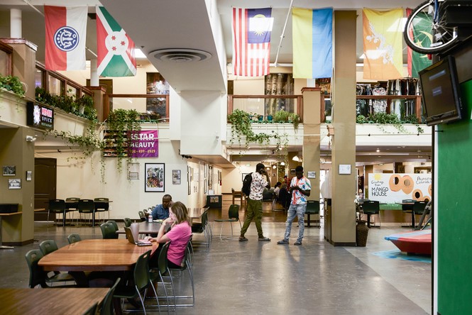 A food hall with many flags from different nations hanging and people sitting at large tables.