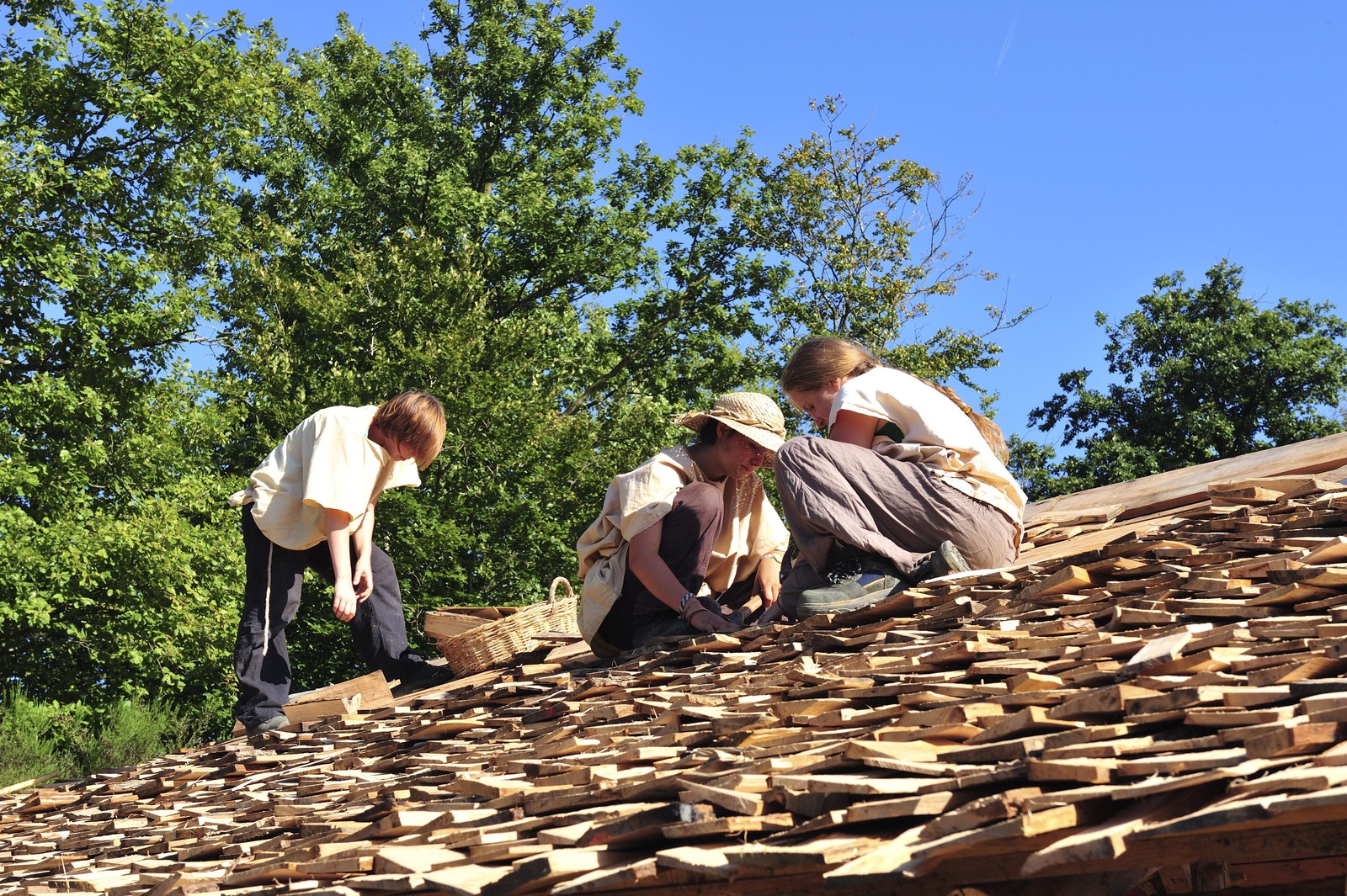 Several young people work on a wood-shingled roof.