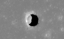 The opening to a lunar pit forms a black crescent on a gray landscape.